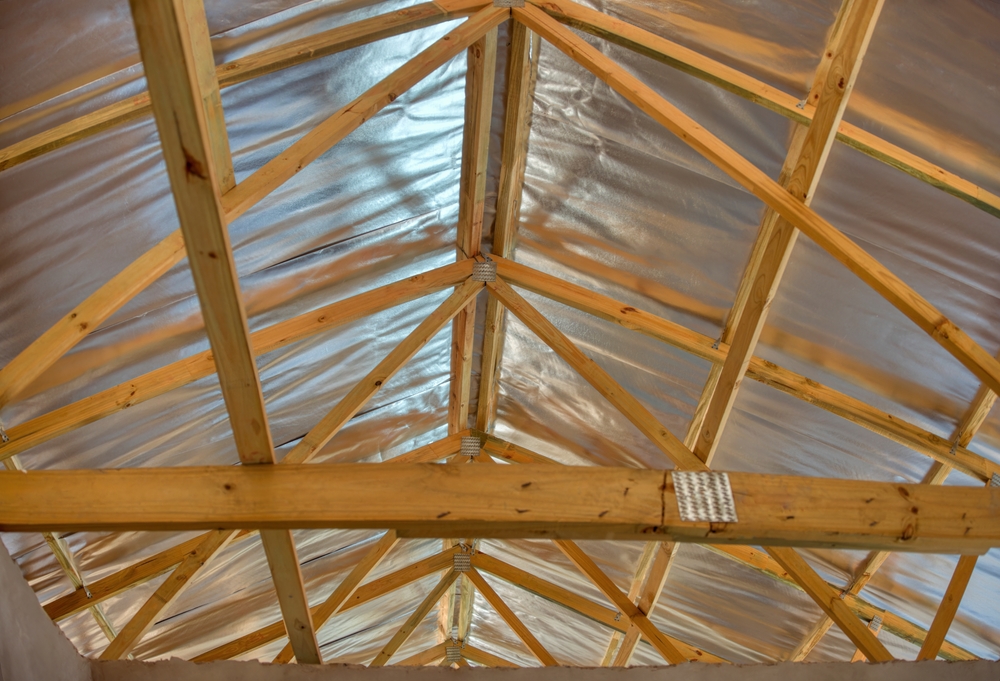 A wood-framed attic that is being insulated with thermal foil
