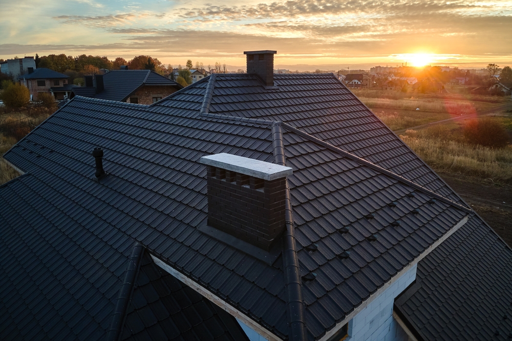 A sunset over the roof of a home with black slate tiles and a chimney