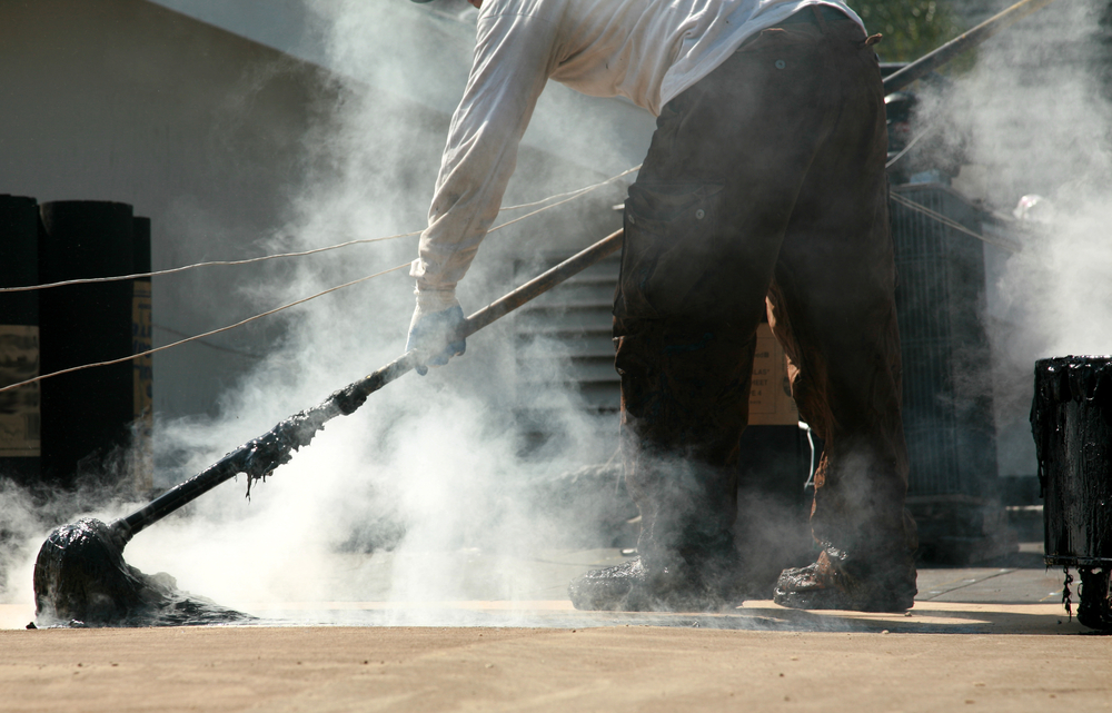 A worker spreads hot tar on a built up roof using a large mop
