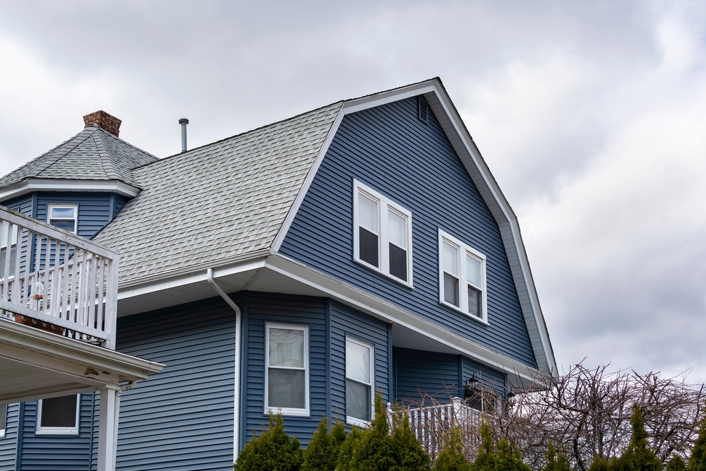 A blue house with a classic gambrel style roof and black asphalt shingles