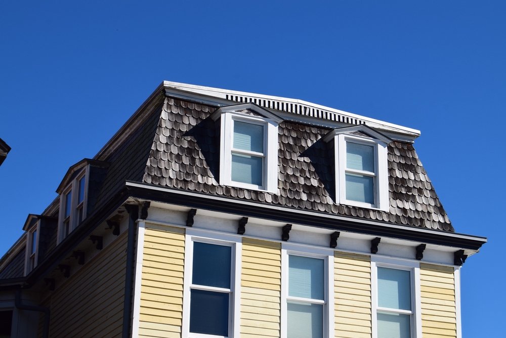 A 70's style Mansard roof with two dormers and worn wood shingles