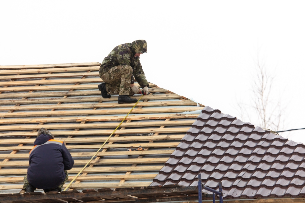 Two roofing contractors repairing a roof made of metal panels