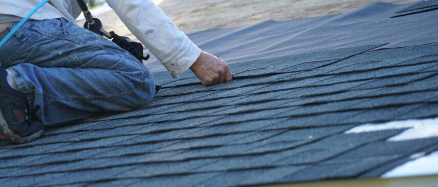 A worker installing new asphalt shingles on a home roofing project