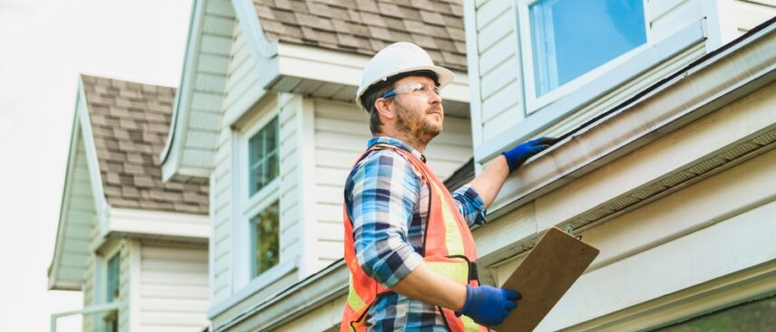 A roof inspector on a ladder inspecting a residential roof