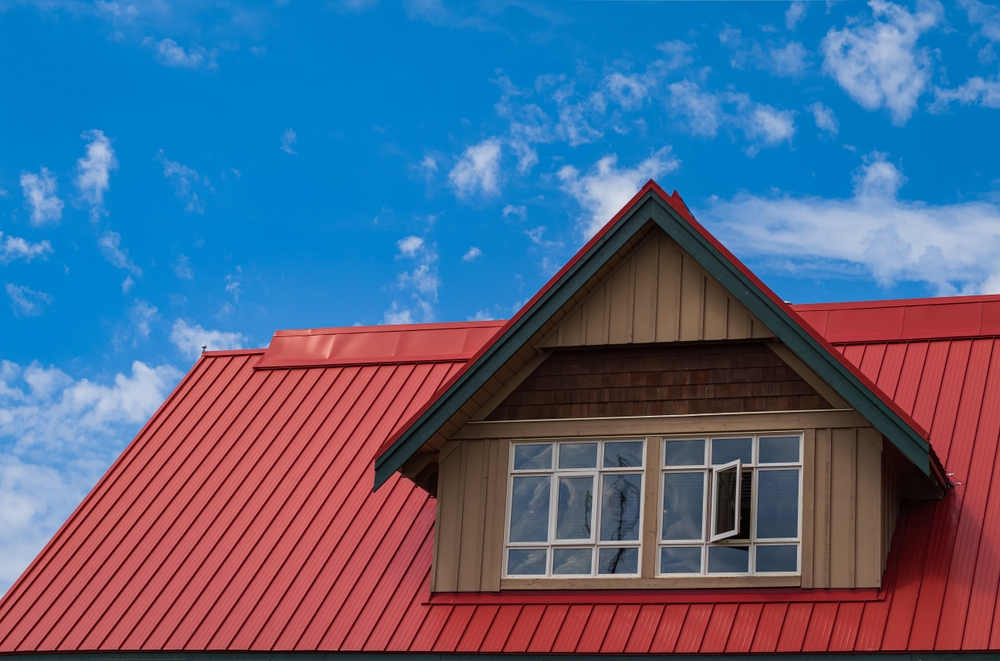 A house with a red metal paneled roof and one large dormer