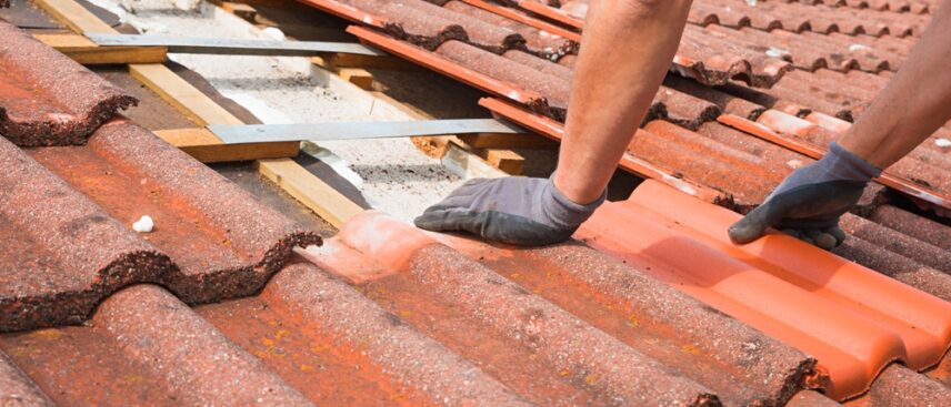 A contractor replaces a red clay tile on a home roofing project