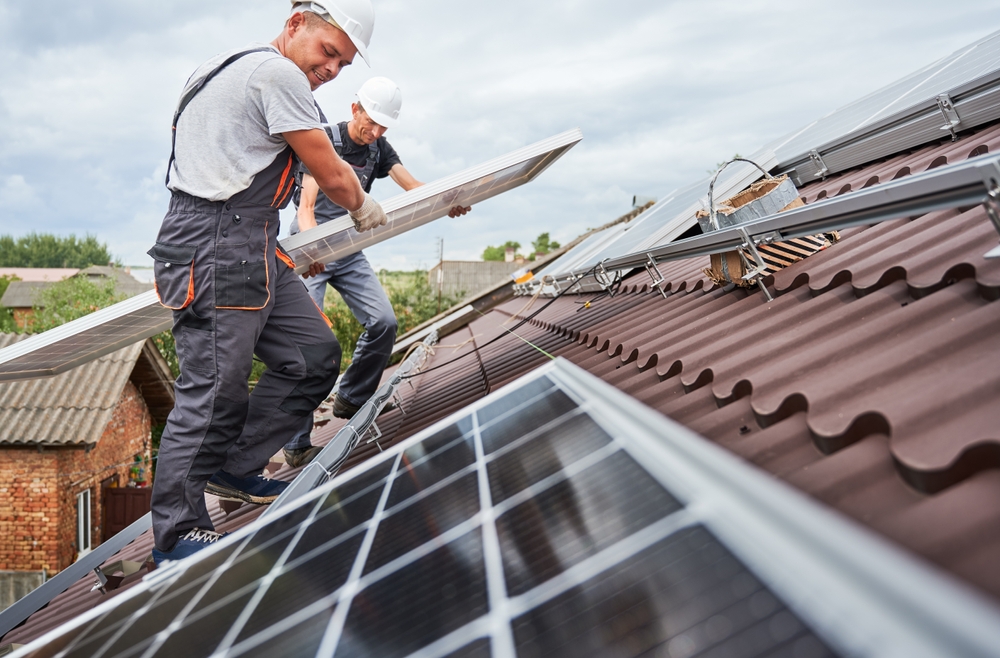 Two workers carefully installing a solar panel on a residential home roof